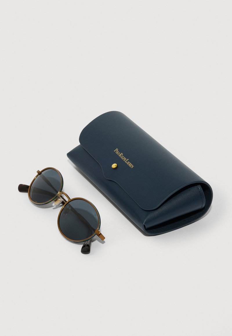 Lunettes de soleil rondes avec verres foncés, accents dorés, et un élégant étui en cuir bleu marine comprenant une fermeture à pression et un logo en relief.