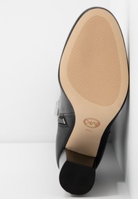 Černá kožená boty zobrazená ze spodní strany s béžovou podrážkou, zipem na boku a širokým podpatkem na bílém pozadí.