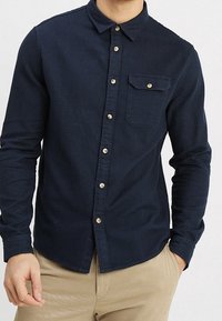 Marinblå skjorta med knappar, tillverkad av bomull, med en bröstficka, kontrasterande gyllene knappar och en klassisk kragsdesign.