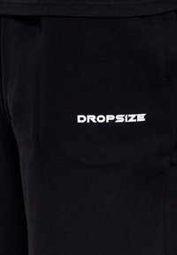 Vêtement en tissu noir avec texte blanc en gras « DROPSIZE » imprimé à l'avant près de la zone de la hanche.