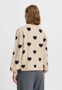 Beiger Pullover mit schwarzen Herzmustern, aus weichem Strickmaterial gefertigt. Hat einen runden Halsausschnitt und einen lässigen Schnitt mit gerippten Bündchenärmeln.