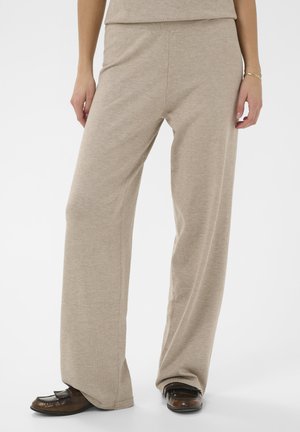 Beige Hosen mit weitem Bein aus weichem Stoff, ausgestattet mit einem taillierten Bund. Kombiniert mit braunen Schuhen, die das entspannte Design hervorheben.