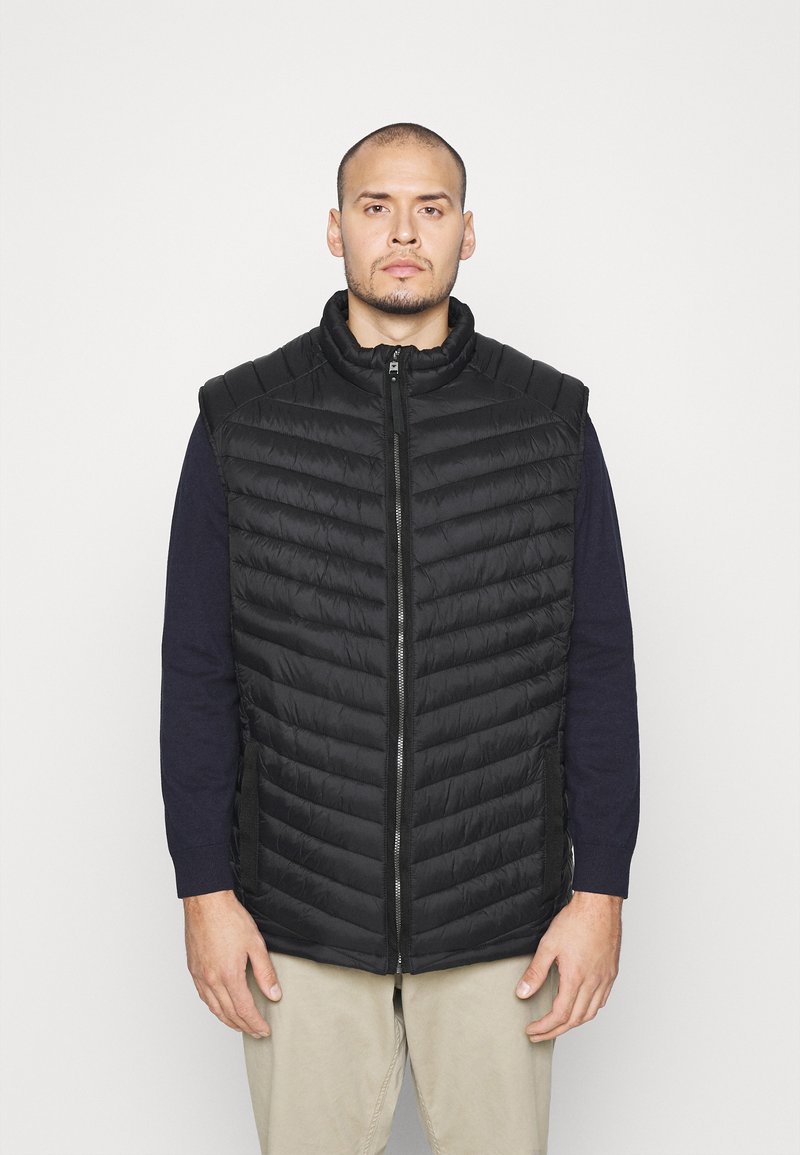 Gilet imbottito nero con colletto alto, caratterizzato da motivi a righe orizzontali, una zip frontale e tasche laterali. Indossato sopra una camicia blu navy.