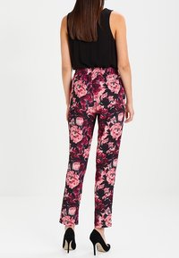 Bloemenbroek met een zwarte basis en grote roze en bordeauxrode bloempatronen, elastische tailleband, rechte pijpen, gecombineerd met zwarte hakken.