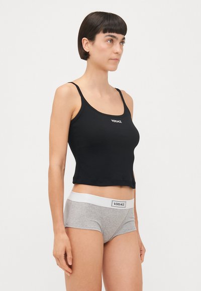 Fekete, testhezálló crop top vékony pántokkal, amelyen egy fehér "VERSACE" logó található. Szürke boxer alsóval párosítva, amelynek fehér derékrésze van.