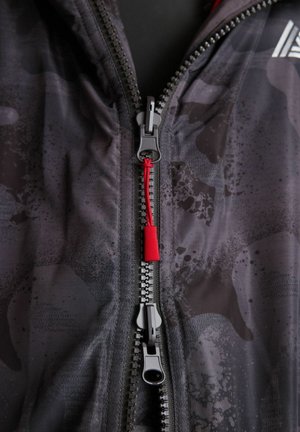 Mustükk zipiga jakk, millel on kamuflaažimuster, punase tõmbluku ja metallist detailidega. Pehme tekstuur ja kerge materjal.