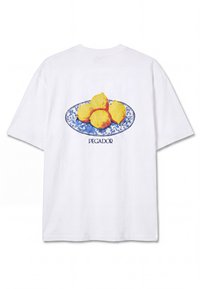 T-shirt blanc avec une assiette florale bleue tenant quatre citrons jaunes et le mot « PEGADOR » imprimé en dessous dans le dos.