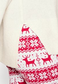 Top in crema con texture a coste, abbinato a leggings rossi e bianchi con design di renne e fiocchi di neve.