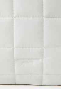 Tissu matelassé blanc avec couture carrée et texte brodé « ARKK COPENHAGEN EST. 2015 » centré sur un carré.