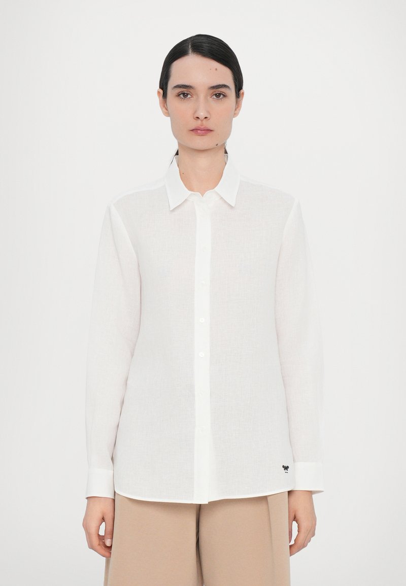 White button-up shirt made of linen with long sleeves, a collar, and an embroidered black accent on the hem. Smooth texture and relaxed fit.