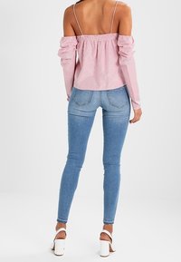 Punavalkoraidallinen, hartioita paljastava paita, jossa on hartiahiat, yhdistetty vaaleansinisiin kapeisiin farkkuihin ja valkoisiin block-korkoisiin sandaaleihin.