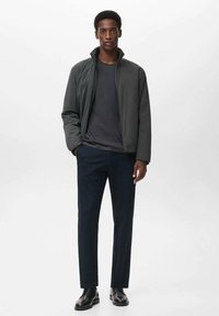 Donkergrijze zip-up jas met staande kraag, zwarte shirt eronder, marineblauwe broek en zwarte schoenen. Eenvoudig ontwerp en slim fit.