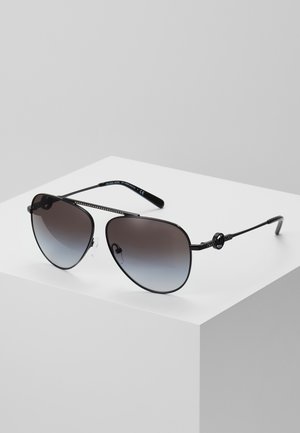 Schwarze Aviator-Sonnenbrille aus Metall mit verlaufenden dunklen Gläsern und dekorativen Seitendetails, auf einem weißen Podest vor grauem Hintergrund liegend.
