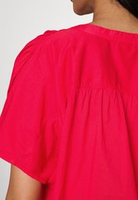 Lys pink bluse med korte, sammensnørede ærmer og en afslappet pasform med bageste plisseringer, lavet af letvægtsstof.