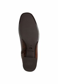 Suola di scarpe in pelle marrone con un battistrada in gomma testurizzato, forma curva e marchio in rilievo. Contiene un pulsante per la regolazione della misura.
