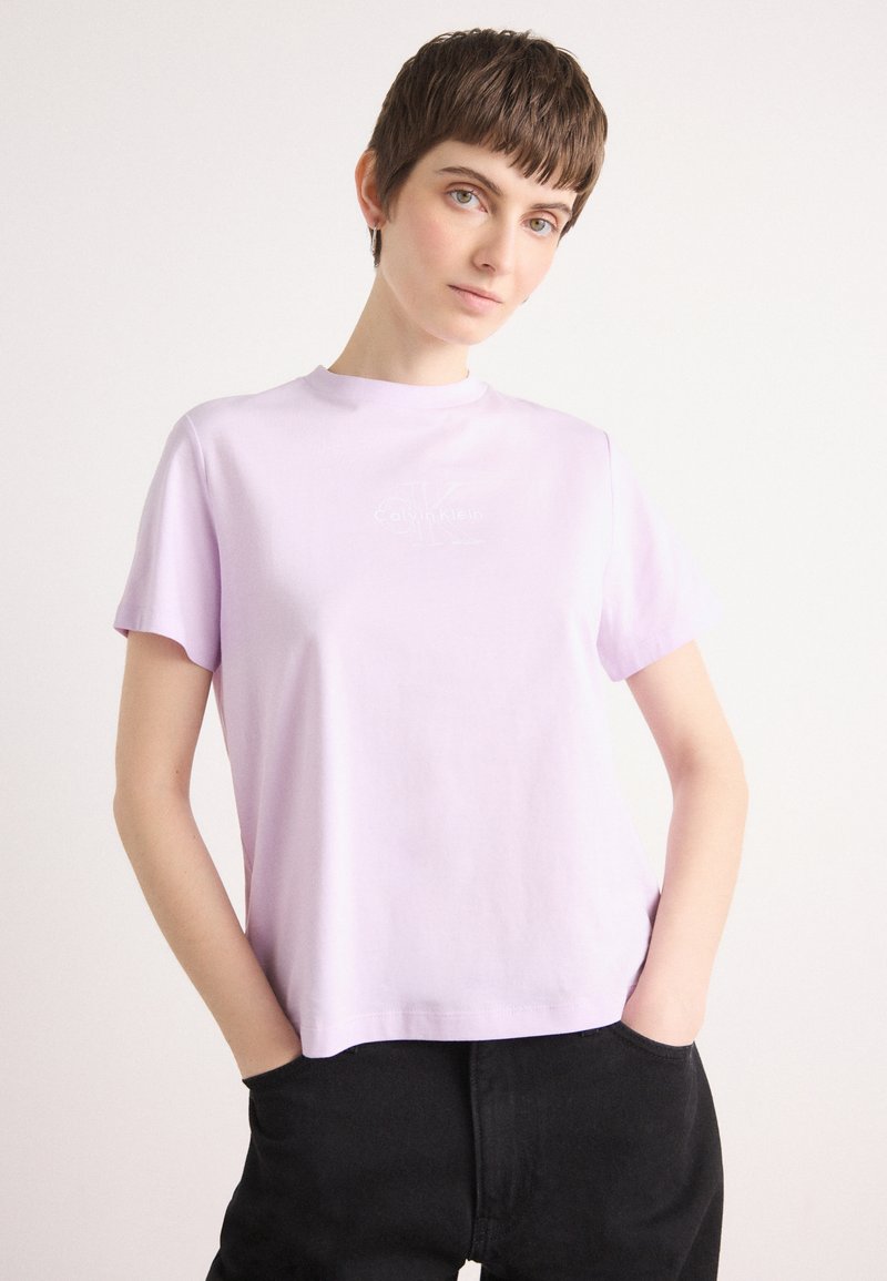Camiseta de algodón lila con mangas cortas y cuello redondo, que presenta un logo tonal de Calvin Klein en el centro, con una textura suave.