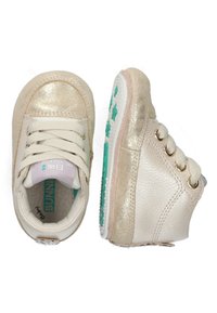 Zapatillas altas de color crema con acentos dorados metálicos, cordones y suelas de goma texturizada que presentan un patrón de estrellas en color teal.
