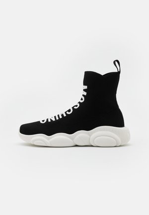 Czarny wysokogatunkowy sneaker w formie skarpetki z grubą, białą, teksturowaną podeszwą i białym napisem nazwy marki biegnącym pionowo wzdłuż boku.