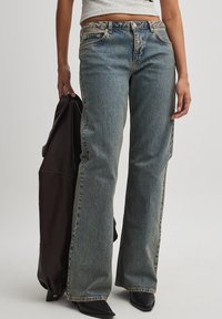 Vaqueros de denim azul claro con un corte relajado, que presentan una cintura de altura media, costuras visibles y un diseño clásico de cinco bolsillos. También hay calzado negro y una chaqueta oscura.