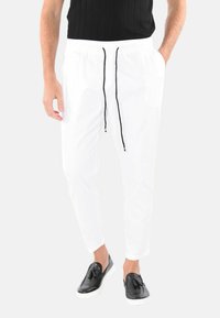 Pantaloni bianchi a sigaretta con elastico in vita e cordino nero, abbinati a una maglietta nera e a scarpe nere senza lacci. Texture liscia.