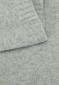 Lys grå strikket stoff som viser en myk tekstur, med vekslende ribbede og flate mønstre, med en fuzzy finish.