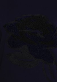 Fialová tkanina s texturovaným černým květinovým vzorem, s pečlivými detaily na okvětních plátcích a listech, vytvářejícími hloubku a kontrast.