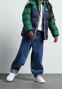 Prošívaná bunda v zelené a námořnicky modré barvě, s zipem a kapucí. Kombinována s volnými modrými džínami a bílými teniskami.