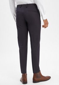 Marineblaue, taillierte Hosen mit Slim Fit, mit flachem Vorderteil und zwei Gesäßtaschen, getragen mit braunen Knöchelschuhen.