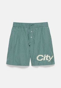 Boxer à carreaux verts et blancs avec des boutons à l’avant et un cordon, avec le mot "City" imprimé sur la jambe droite.