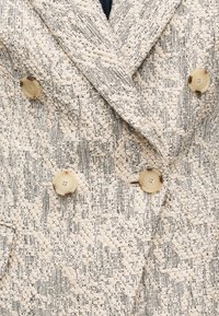 Κρεμ και μαύρο υφασμάτινο σακάκι με υφή, με μεγάλα μπεζ κουμπιά και διπλό γιακά με λεπτομέρειες.