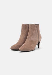 Stivaletti alla caviglia in suede beige con punta appuntita, pannelli laterali elastici e tacco sottile di 5 cm. Texture liscia con dettagli di cuciture minimali.
