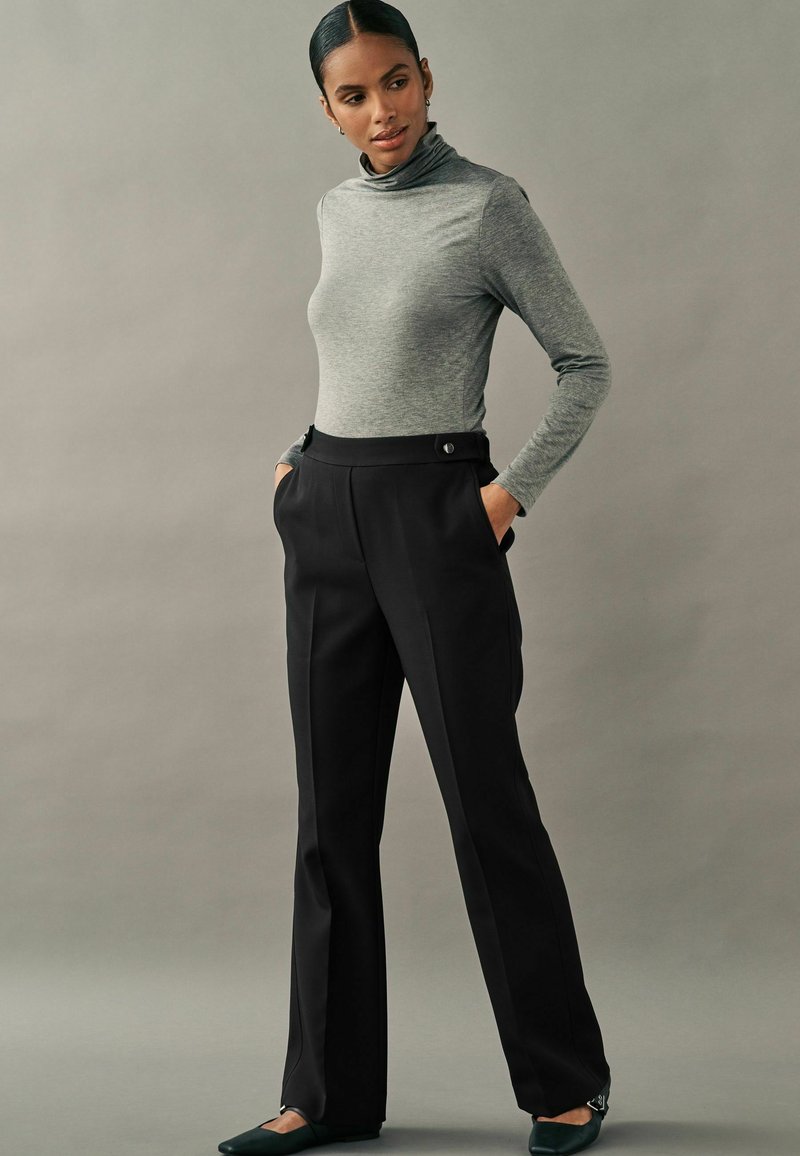 Haut à manches longues gris avec col roulé associé à un pantalon noir taille haute doté de poches avant et d'accents en bouton. Design ajusté.