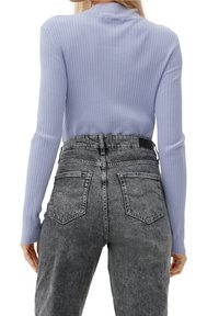 Jasnofioletowa prążkowana bluzka z długim rękawem w połączeniu z wysokim stanem szarymi dżinsami z dwoma tylnymi kieszeniami i fakturowanym wykończeniem.