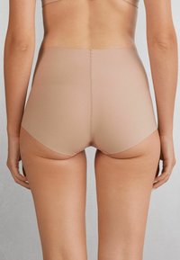 Nude sömlösa högmidjade underkläder med en slät yta, utformade för komfort. Har låg skärning på benen och minimala sömdetaljer.