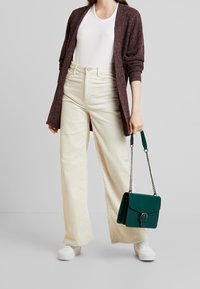 Tumman viininpunainen ylisuuri neuletakki, valkoinen T-paita, kermaiset corduroy-tekstiiliset leveät housut, valkoiset lenkkarit ja vihreä käsilaukku ketjuhihnalla.