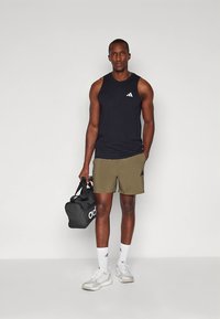 Μαύρο αθλητικό φανελάκι με λευκό λογότυπο, χακί σορτς, λευκά αθλητικά παπούτσια και μαύρη αθλητική τσάντα με λευκό λογότυπο.