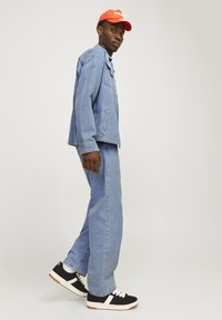 Vaate denim-takki ja leveät farkut vaaleansinisinä, yhdistettynä kirkkaan oranssiin lippikseen. Mustat lenkkarit valkoisilla yksityiskohdilla. Tasainen pinta.