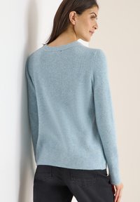 Helle blaue, gerippte Strickjacke mit langen Ärmeln und runder Ausschnittform, ausgestattet mit einem strukturierten Stoff und figurbetonter Saumlinie.