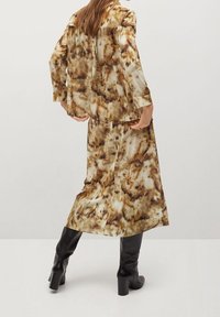 Brauner und beige bedruckter Anzug aus glattem Stoff, bestehend aus einem langen Jacket und einem Rock mit fließender Silhouette und übergroßem Schnitt.