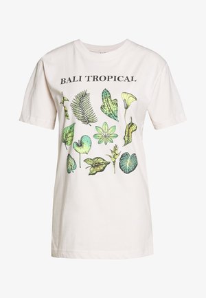 Világos bézs pamut póló, amely különféle zöld levelek növényi mintájával díszített, a minta felett fekete "BALI TROPICAL" felirattal.
