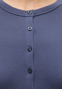 Gros plan d'une chemise en tissu côtelé bleu avec quatre petits boutons foncés et un col arrondi.