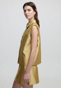 Gold satin sleeveless top with a collar and button-down front, paired with a matching mini skirt, smooth texture, and relaxed fit.