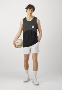 Juoda ir pilka sportinė tankų marškinėliai su apvaliais kaklo išpjovomis ir baltos šortai. Modelis laiko krepšinį, vilkėdamas baltas kulkšninės kojines ir sportinius batus.