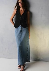 Sort vest med knapper, parret med en lyseblå denim maxi-nederdel med sidelommer. Sorte stroppestiletter fuldender looket.