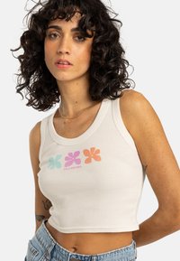 Débardeur blanc à côtes avec un graphisme floral coloré en bleu, rose, orange et violet. Design cropped avec un col rond.