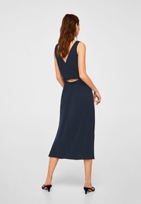 Navy blue, sleeveless dress with a deep V-back and cut-out detail at the waist. Made from a smooth, lightweight fabric that drapes to mid-calf.