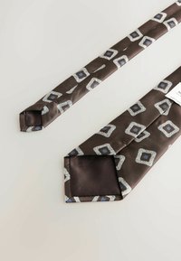 Brown silk tie featuring geometric patterns in light gray and blue, with a smooth texture and pointy tip design. Tag visible at the end.