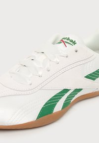 Baskets blanches Reebok avec des bandes vertes, des lacets blancs en satin, des accents en daim beige et une semelle en gomme.