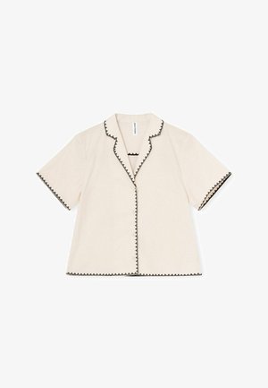 Majica s kratkimi rokavi iz kremaste tkanine z črnimi cik-cak obrobami ob ovratniku, manšetah in gumbni plati. Zapenjanje z gumbi spredaj.