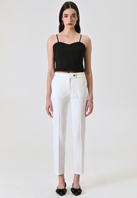 Top noir court avec de fines bretelles, associé à un pantalon blanc ajusté avec un bouton unique et une finition lisse. Les chaussures sont noires avec des nœuds.